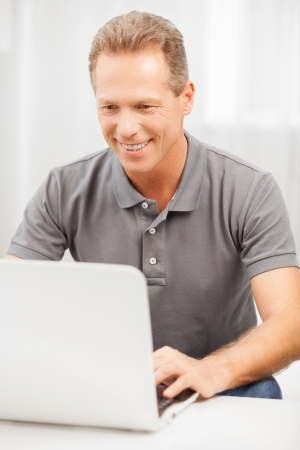 Man surfing web. Cheerful grey hair man in polo shirt using laptop and smilingの写真素材