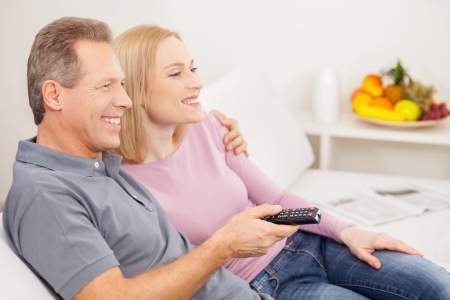 Watching TV together. Side view of cheerful mature couple sitting together and watching TVの写真素材
