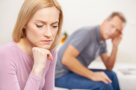 Family problems. Side view of depressed mature woman holding hand on chin while sad man sitting on backgroundの写真素材