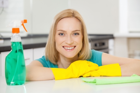 Cheerful housewife. Mature blond hair woman in yellow gloves leaning at the table and smilingの写真素材