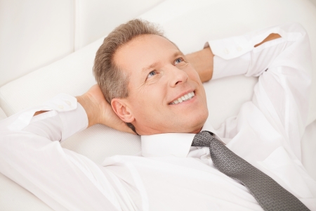 Dreamy businessman. Cheerful grey hair man in shirt and tie lying on bed and smiling の写真素材