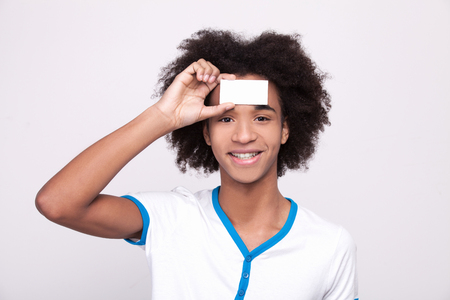 Copy space on my forehead. Cheerful African teenager holding plastic card at his forehead and looking at camera while standing isolated on grey の写真素材