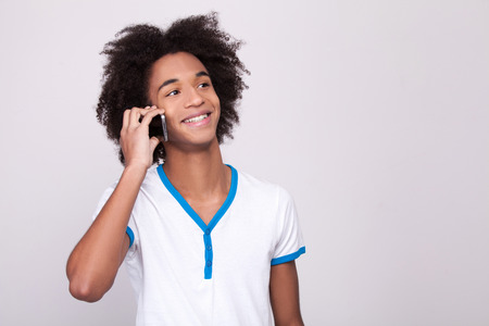 Carefree talk. Cheerful African teenager working on digital tablet and smiling while standing isolated on grey の写真素材