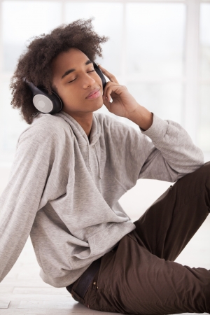 My favorite music. Smiling African teenager in headphones listening to the music and keeping eyes closed while sitting on the floorの写真素材