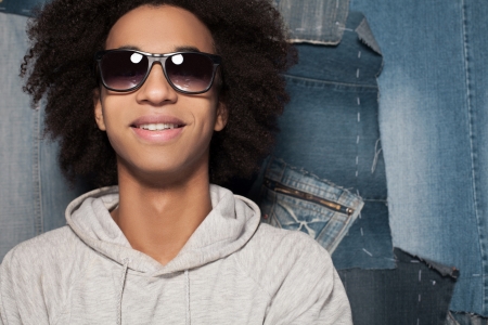 Young and casual. Cheerful African man in sunglasses standing against jeans backgroundの写真素材