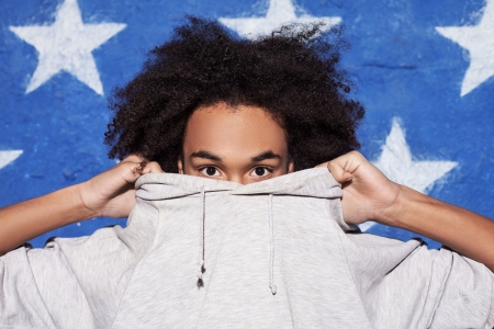 Cool and young. Teenage African boy hiding his face in his clothingの写真素材