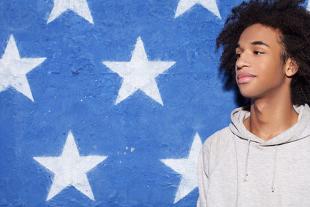 Be cool! Young African man standing against American flag and looking awayの写真素材