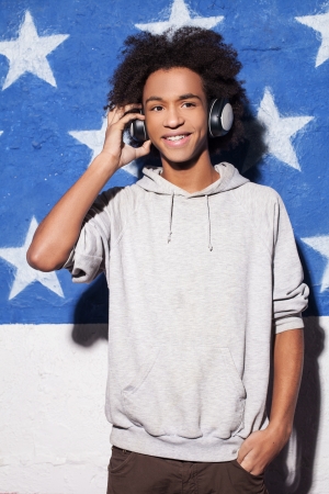 Enjoying music. Cheerful young African man in headphones standing against American flag and listening to the musicの写真素材