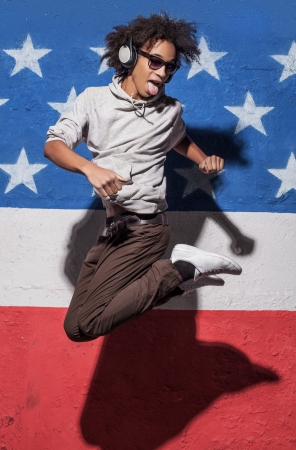 Jump! Cheerful young African man in headphones jumping against American flagの写真素材