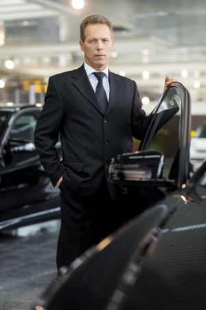 My brand new car. Confident mature grey hair man in formalwear holding hand on opened car door and looking at cameraの写真素材
