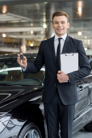 Good choice! Handsome young classic car salesman standing at the dealership and holding a keyの写真素材