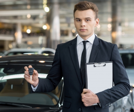 Here is your key! Confident young classic car salesman standing at the dealership and holding a keyの写真素材