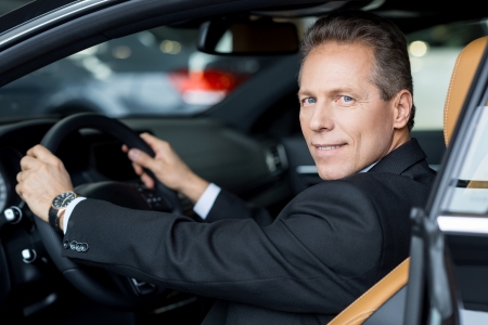 I love this car. Side view of cheerful senior man in formalwear sitting in car and looking over shoulderの写真素材