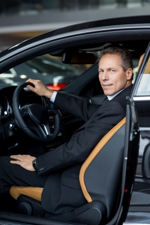 I love my new car. Side view of confident senior man in formalwear sitting in car and smiling at cameraの写真素材