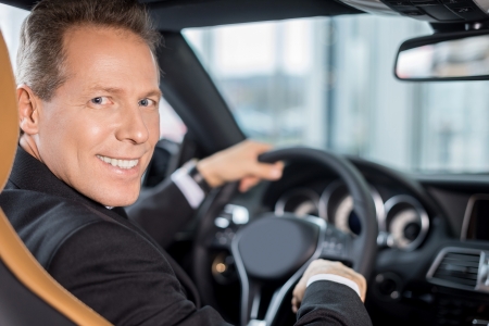 Happy car owner. Rear view of confident senior man in formalwear sitting on drivers place in car and looking over shoulderの写真素材