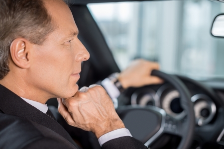 Confident and successful. Confident mature man in formalwear sitting on drivers place in car and looking awayの写真素材