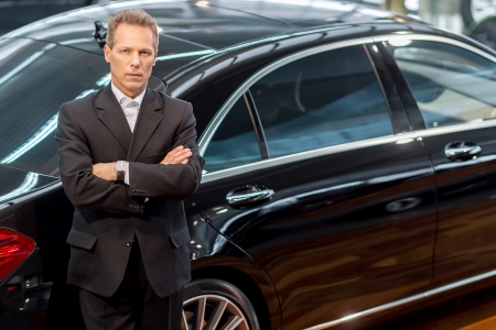 I love luxury cars. Top view of confident grey hair man in formalwear leaning at the car and looking at camera