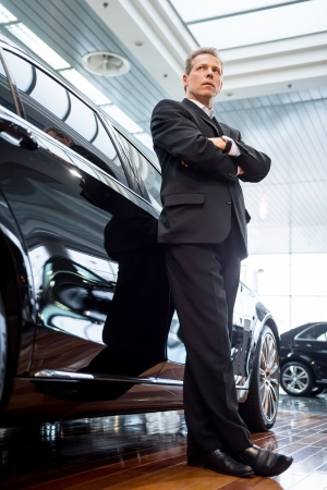 Living a luxury life. Low angle view of confident grey hair man in formalwear leaning at the car and looking awayの写真素材