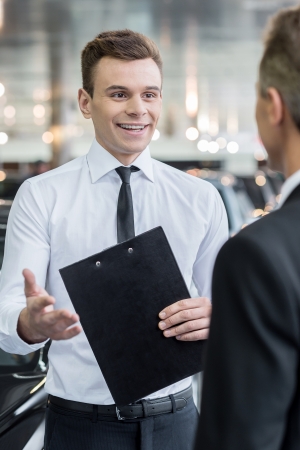 Salesman and customer. Handsome young classic car salesman talking to a customer and smilingの写真素材