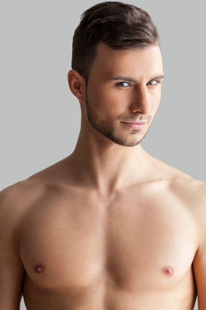 Feeling flirty. Handsome young muscular man looking at camera while standing isolated on grey backgroundの写真素材