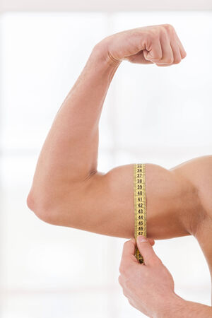 Perfect bicep. Cropped image of muscular man measuring his bicep with measuring tapeの写真素材