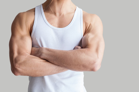 Strong and healthy body. Cropped image of muscular man keeping arms crossed while standing isolated on grey backgroundの写真素材