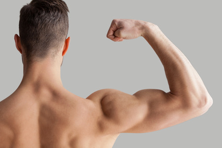 Showing his perfect biceps. Rear view of young muscular man showing his biceps while standing isolated on grey backgroundの写真素材