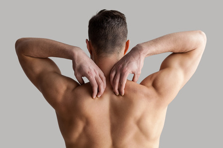 Muscular man. Rear view of young muscular man touching his shoulders while standing isolated on grey backgroundの写真素材