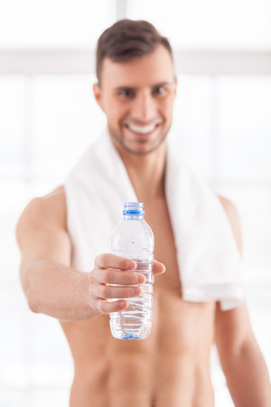 Get refreshed! Cheerful young muscular man holding a bottle with water in his hand and smilingの写真素材