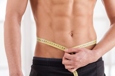 Always in good shape. Cropped image of muscular man measuring his waist with measuring tapeの写真素材