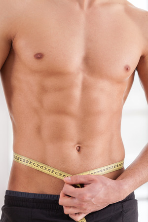 Always in perfect shape. Cropped image of young muscular man measuring his waist with measuring tapeの写真素材