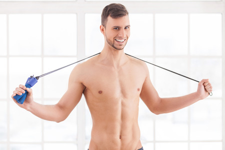 Man with jumping rope. Young muscular man holding a skipping rope on his shoulders and smiling at cameraの写真素材