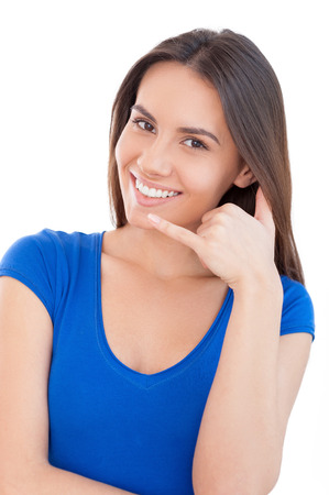 Call me! Beautiful young smiling woman looking at camera and gesturing while standing isolated on whiteの写真素材