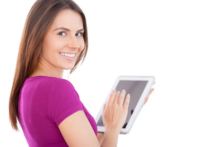 Technologies become easier. Cheerful young woman using digital tablet and looking over shoulder while standing isolated on whiteの写真素材