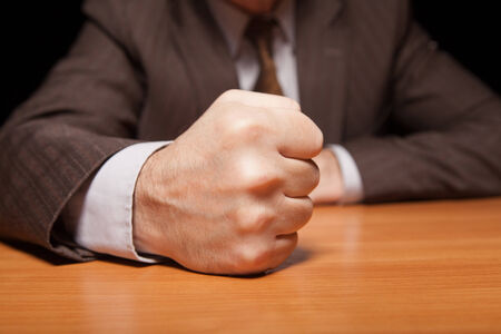 Close-up of man in formal wear holding fist on the table and isolated on blackの写真素材