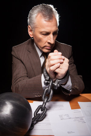 Frustrated senior man in formal wear sitting at his working place and looking at camera while...
