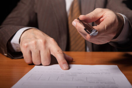 man in formal wear giving a pen to you and pointing a document while isolated on black background の写真素材