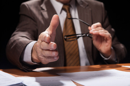 man in formal wear sitting at his working place and stretching out his hand for shaking while isolated on black background の写真素材