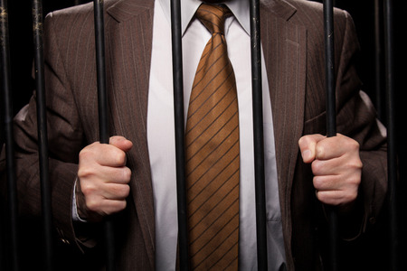 man in formal wear standing behind a prison cell while isolated on black background の写真素材