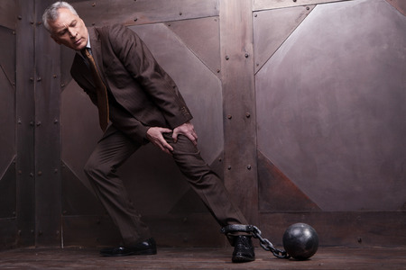 grey hair senior man in formal wear trying to go with the shackles on his legの写真素材