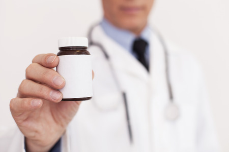 doctor in white uniform stretching out a medicine bottle and while standing isolated on whiteの写真素材