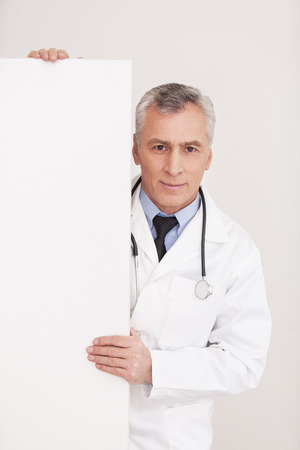 Senior grey hair doctor in uniform looking out of copy space and smiling while isolated on whiteの写真素材