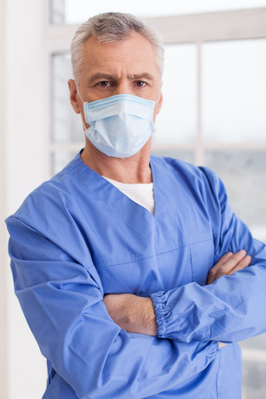 Portrait of senior grey hair doctor in surgical mask looking at cameraの写真素材