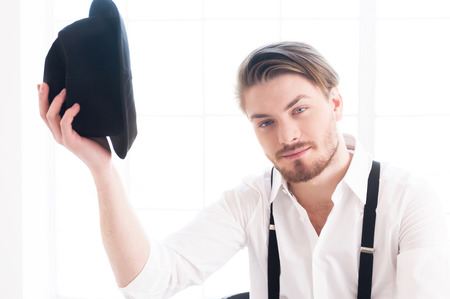 Nice to meet you! Handsome young man in shirt and suspenders holding a hat near head and looking at camera with smileの写真素材