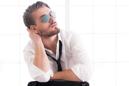 Handsome and confident man. Thoughtful young man in sunglasses holding head in hand and looking away while sitting on the chairの写真素材