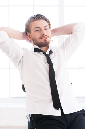 Total relaxation. Handsome young man in shirt and tie holding head in hands while sitting on the chairの写真素材