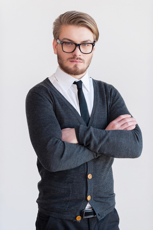 Confident young man. Handsome young man in glasses keeping arms crossed and while standing against grey backgroundの写真素材