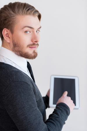 Man with digital tablet. Rear view of handsome young man holding a digital tablet and looking over shoulder while standing against grey backgroundの写真素材
