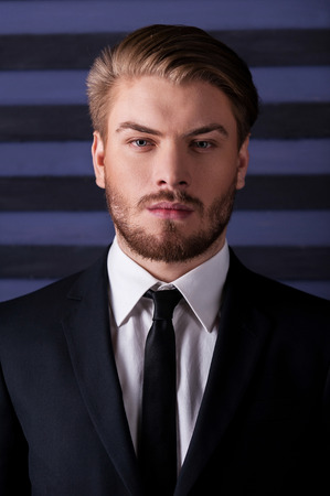 Young and confident. Portrait of handsome young man in formalwear looking at camera while standing against striped backgroundの写真素材