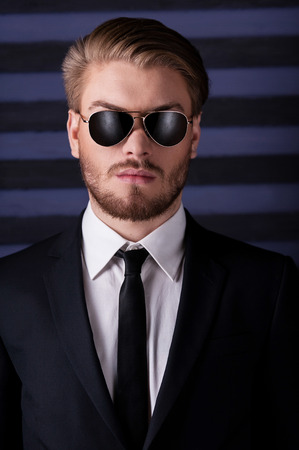 Portrait of confidence and masculinity. Portrait of handsome young man in sunglasses and formalwear looking at camera while standing against striped backgroundの写真素材